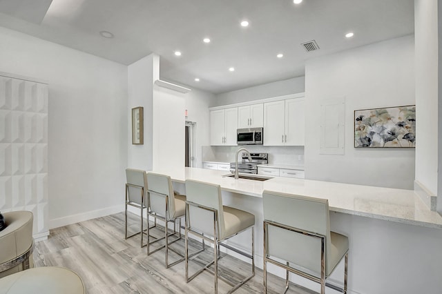 kitchen with sink, a kitchen bar, kitchen peninsula, white cabinetry, and stainless steel appliances