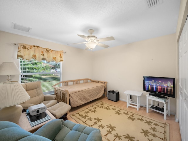 bedroom with ceiling fan, wood-type flooring, a textured ceiling, and a crib