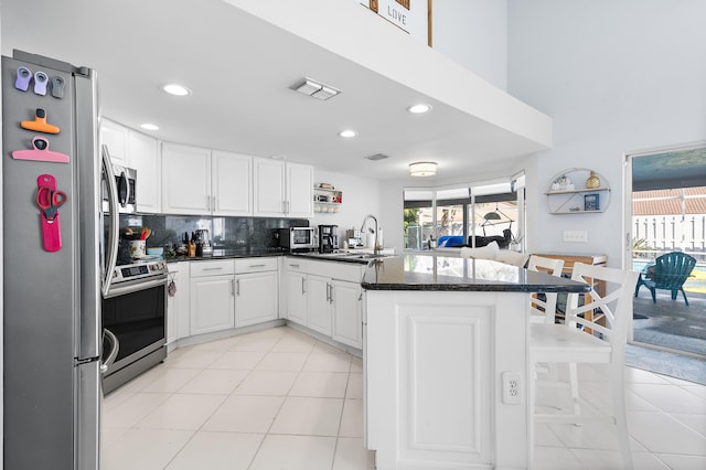 kitchen with kitchen peninsula, appliances with stainless steel finishes, tasteful backsplash, white cabinets, and sink