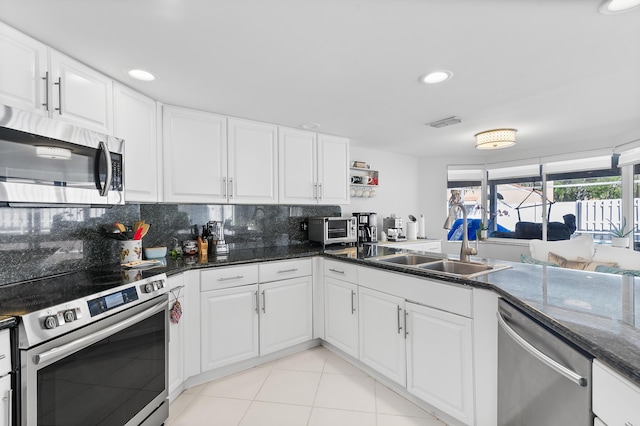 kitchen featuring decorative backsplash, sink, appliances with stainless steel finishes, white cabinets, and dark stone counters