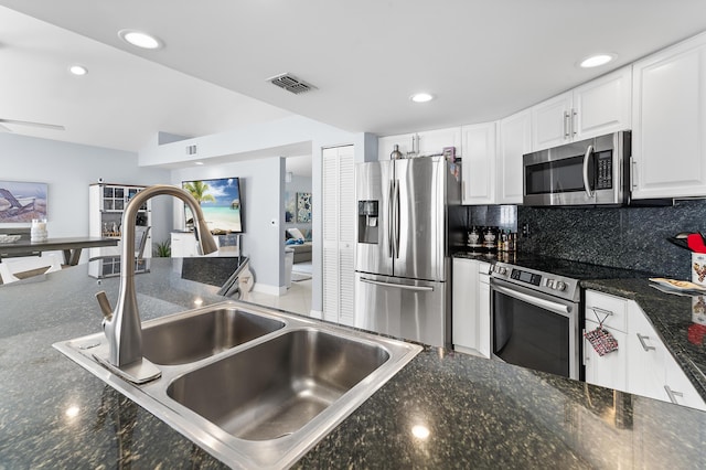 kitchen featuring backsplash, sink, white cabinetry, stainless steel appliances, and dark stone counters