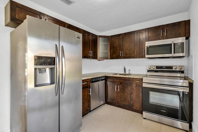 kitchen with appliances with stainless steel finishes, light stone counters, a textured ceiling, sink, and light tile patterned floors