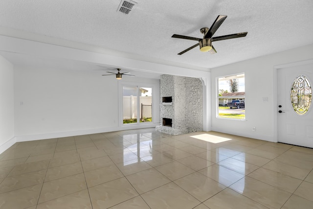 unfurnished living room featuring ceiling fan, a large fireplace, light tile patterned floors, and a textured ceiling