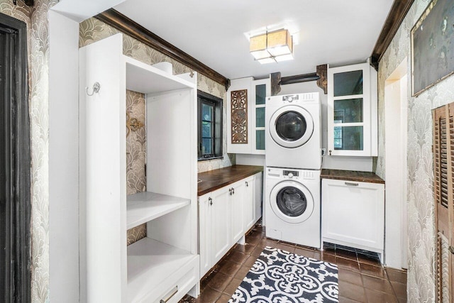 laundry area featuring wallpapered walls, cabinet space, dark tile patterned flooring, and stacked washer / dryer