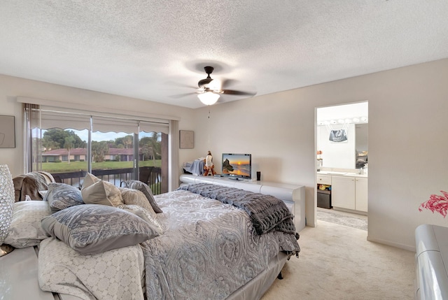 bedroom featuring access to outside, ensuite bath, a textured ceiling, ceiling fan, and light colored carpet