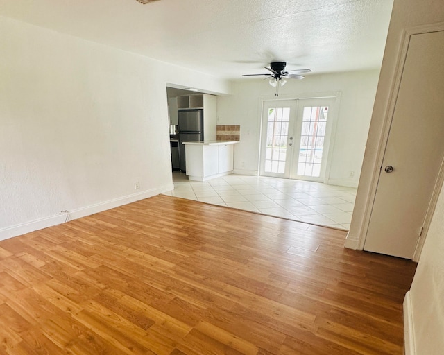 unfurnished living room featuring ceiling fan, french doors, light hardwood / wood-style floors, and a textured ceiling