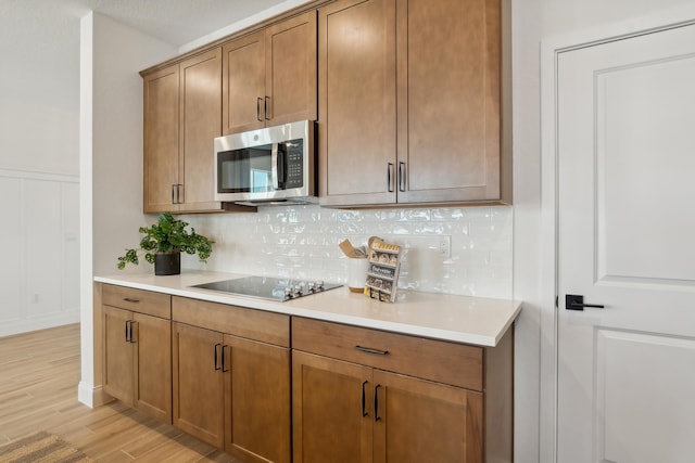 kitchen with light hardwood / wood-style floors, black electric cooktop, a textured ceiling, and tasteful backsplash