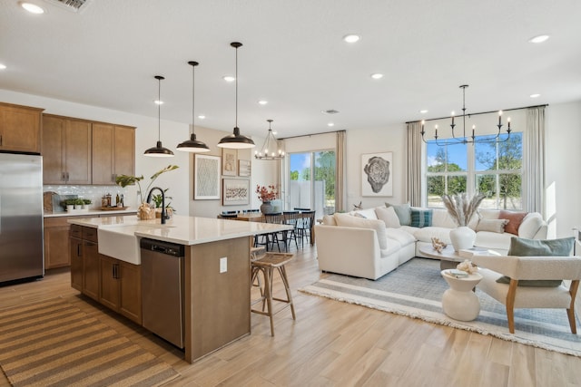 kitchen with a healthy amount of sunlight, stainless steel appliances, hanging light fixtures, and a kitchen island with sink