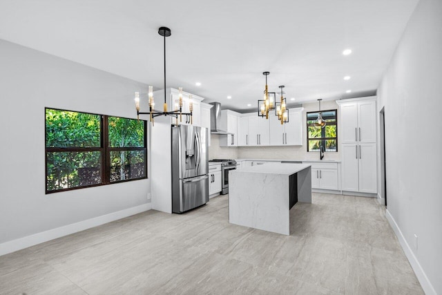 kitchen with appliances with stainless steel finishes, a center island, white cabinetry, wall chimney exhaust hood, and decorative light fixtures