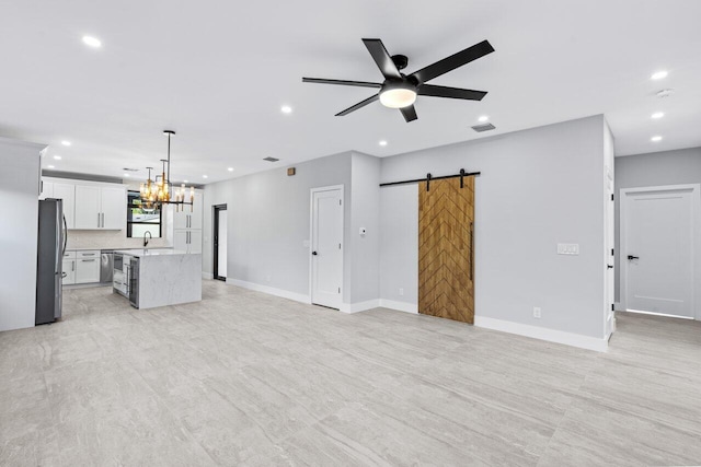 unfurnished living room featuring sink, a barn door, and ceiling fan with notable chandelier