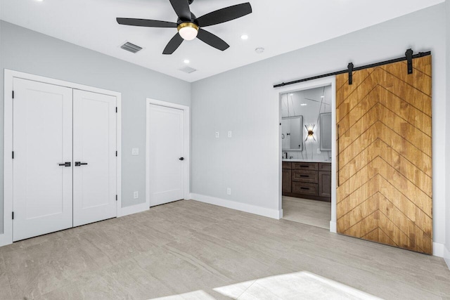 unfurnished bedroom featuring connected bathroom, a barn door, light colored carpet, and ceiling fan