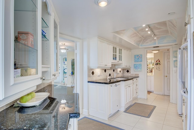 kitchen featuring white cabinetry, dark stone countertops, a tray ceiling, white dishwasher, and decorative backsplash