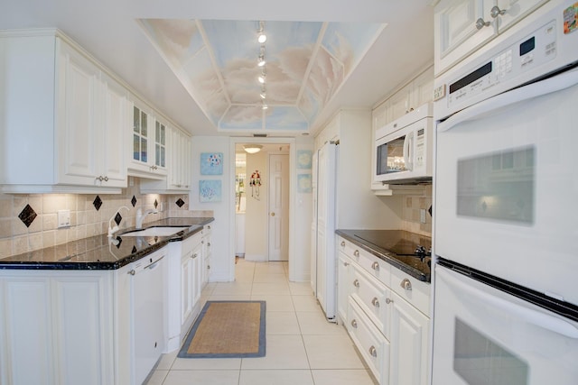 kitchen featuring white appliances, white cabinetry, tasteful backsplash, a tray ceiling, and dark stone counters