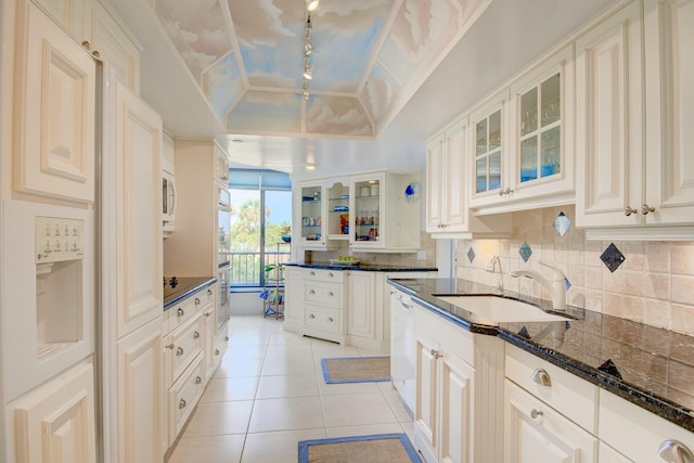 kitchen with light tile patterned floors, sink, dark stone countertops, tasteful backsplash, and a raised ceiling