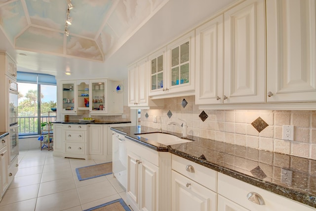 kitchen with light tile patterned flooring, sink, vaulted ceiling, dark stone countertops, and decorative backsplash