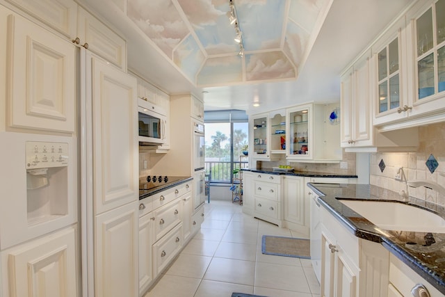 kitchen with dark stone countertops, sink, tasteful backsplash, and a raised ceiling