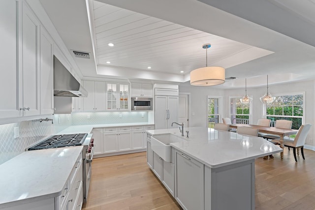 kitchen with built in appliances, white cabinetry, a center island with sink, and sink