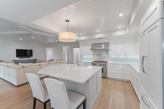 kitchen featuring high end range, wall chimney exhaust hood, pendant lighting, light hardwood / wood-style floors, and white cabinetry