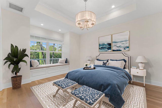 bedroom with a chandelier, light wood-type flooring, crown molding, and a tray ceiling