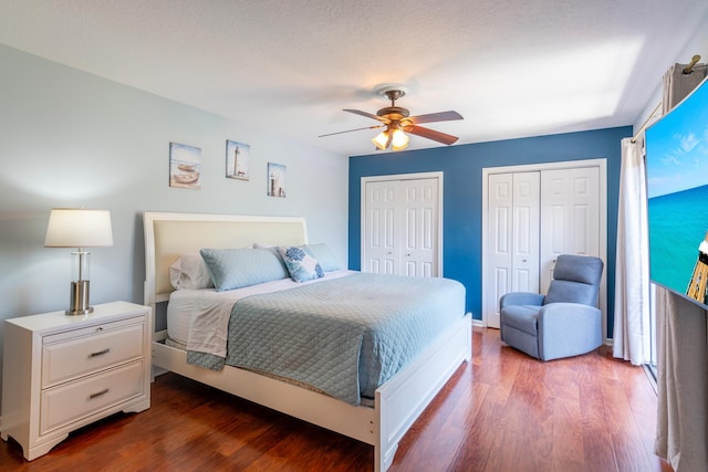 bedroom featuring ceiling fan, wood-type flooring, a textured ceiling, and two closets