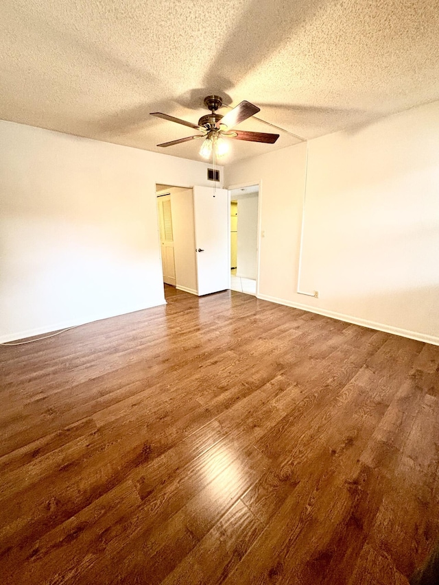 unfurnished room with a textured ceiling, dark wood finished floors, visible vents, and a ceiling fan