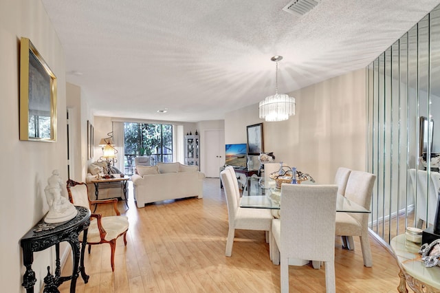 dining space with light hardwood / wood-style floors, a textured ceiling, and an inviting chandelier