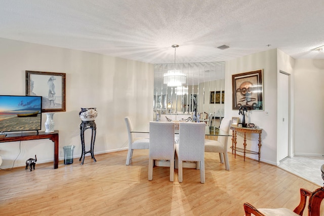 dining area with a textured ceiling, hardwood / wood-style flooring, and an inviting chandelier