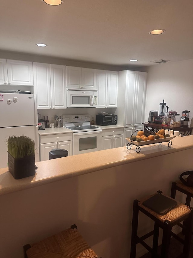 kitchen with white cabinetry, a breakfast bar, and white appliances