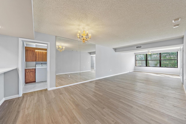 unfurnished living room with washer / dryer, a notable chandelier, a textured ceiling, and light hardwood / wood-style floors