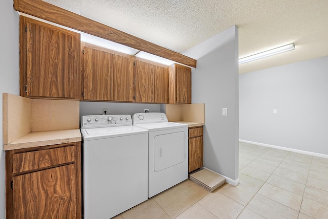 washroom with light tile patterned floors, a textured ceiling, washing machine and dryer, and cabinets