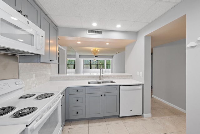 kitchen featuring decorative backsplash, light tile patterned floors, gray cabinetry, sink, and white appliances