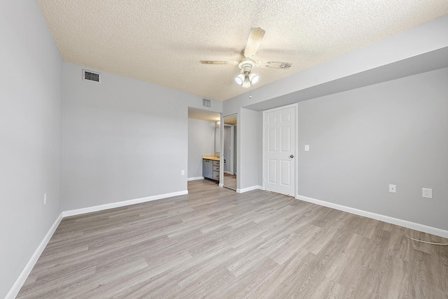 empty room with a textured ceiling, light wood-type flooring, and ceiling fan