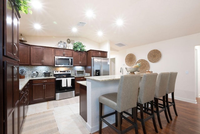 kitchen with a kitchen island, stainless steel appliances, a breakfast bar, vaulted ceiling, and light stone counters