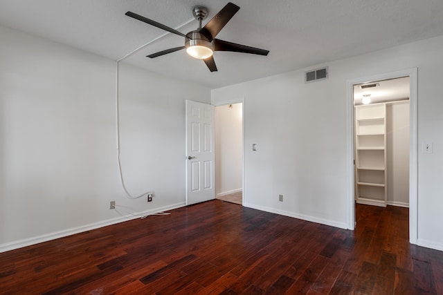 unfurnished bedroom featuring ceiling fan, dark hardwood / wood-style floors, a walk in closet, and a closet