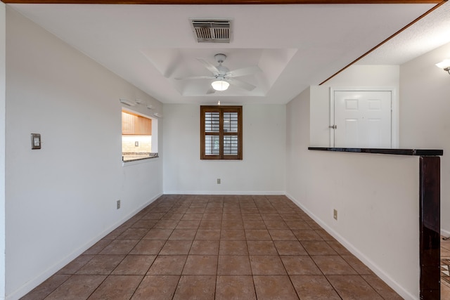 tiled spare room featuring ceiling fan and a tray ceiling