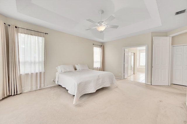 bedroom featuring ensuite bath, light colored carpet, a raised ceiling, and ceiling fan