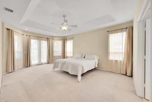 carpeted bedroom with a raised ceiling, multiple windows, and ceiling fan