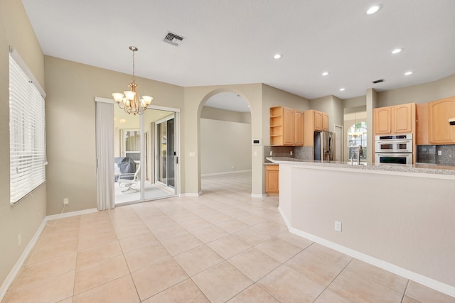 kitchen with light brown cabinets, stainless steel appliances, an inviting chandelier, light tile patterned floors, and tasteful backsplash