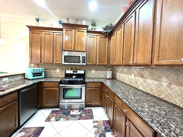 kitchen featuring dark stone counters, crown molding, decorative backsplash, light tile patterned floors, and appliances with stainless steel finishes