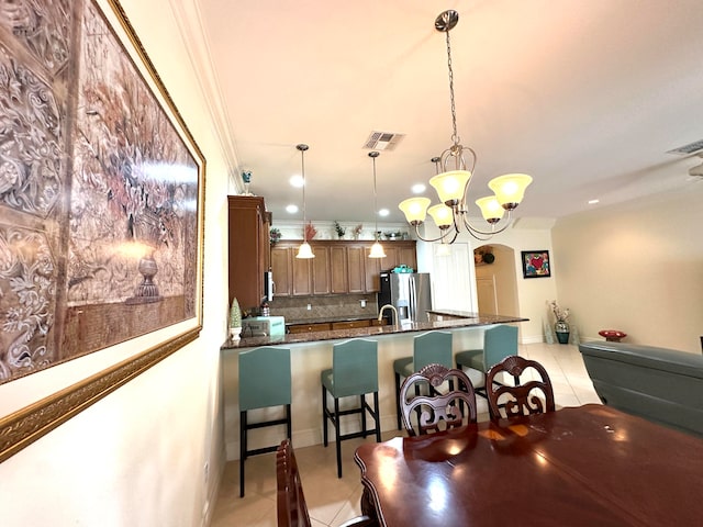 kitchen with an inviting chandelier, stainless steel fridge, decorative light fixtures, light tile patterned floors, and ornamental molding