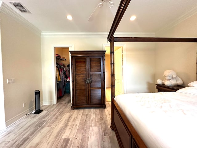 bedroom featuring a spacious closet, ceiling fan, light wood-type flooring, a closet, and ornamental molding