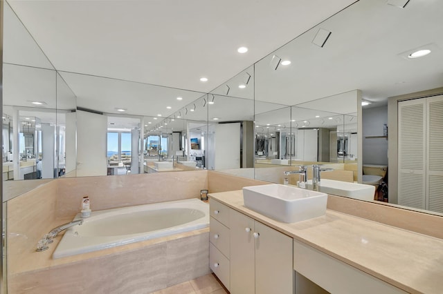 bathroom with vanity, toilet, and tiled bath