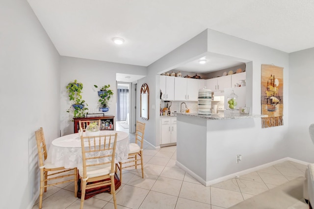 kitchen featuring light stone countertops, white cabinetry, kitchen peninsula, and light tile patterned floors