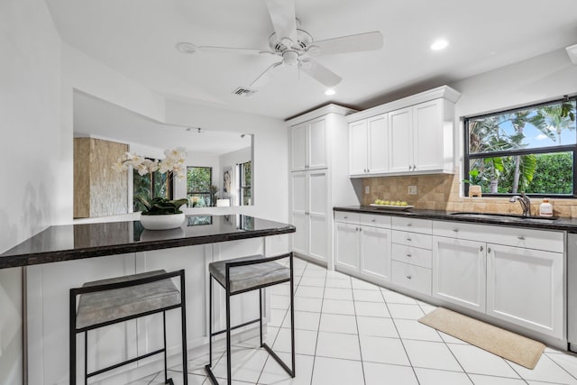 kitchen featuring light tile patterned floors, a sink, white cabinetry, a kitchen breakfast bar, and backsplash