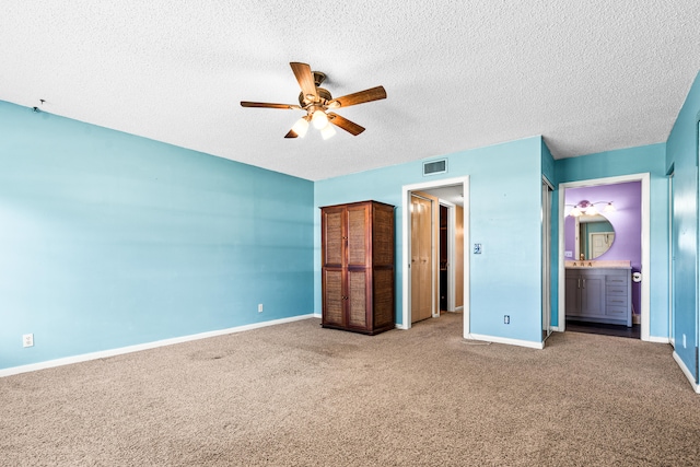 unfurnished bedroom featuring ceiling fan, carpet floors, a textured ceiling, and ensuite bath