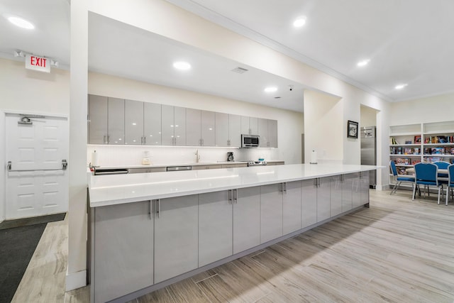 kitchen featuring gray cabinetry, a breakfast bar area, light hardwood / wood-style flooring, ornamental molding, and stainless steel appliances