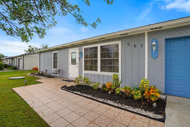 view of exterior entry featuring a patio, a yard, and a garage