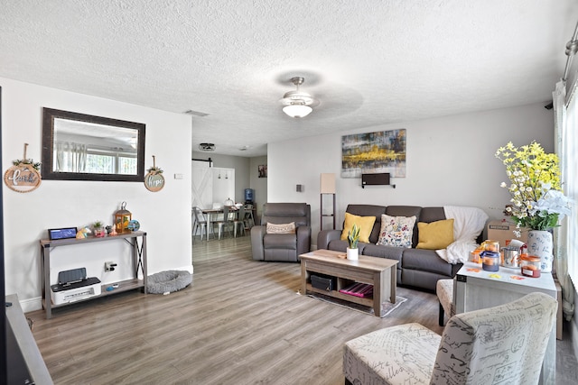 living room featuring a textured ceiling, a barn door, hardwood / wood-style flooring, and ceiling fan