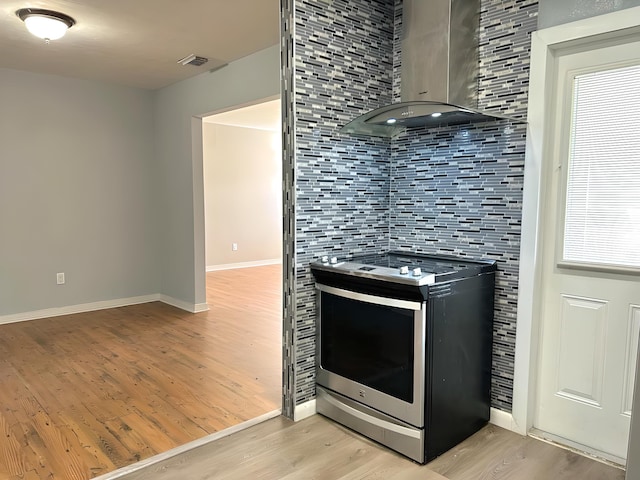 kitchen featuring light hardwood / wood-style floors, wall chimney range hood, backsplash, and stainless steel stove