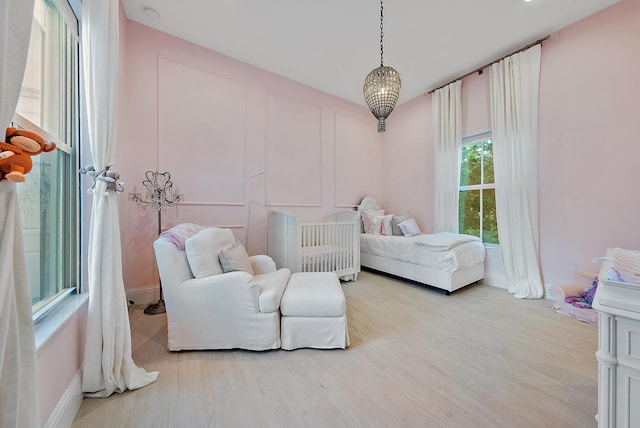 bedroom with light hardwood / wood-style flooring, a chandelier, and a crib